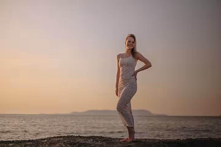 Woman in a floral dress posing on Gouves beach at sunset for a private photoshoot experience.