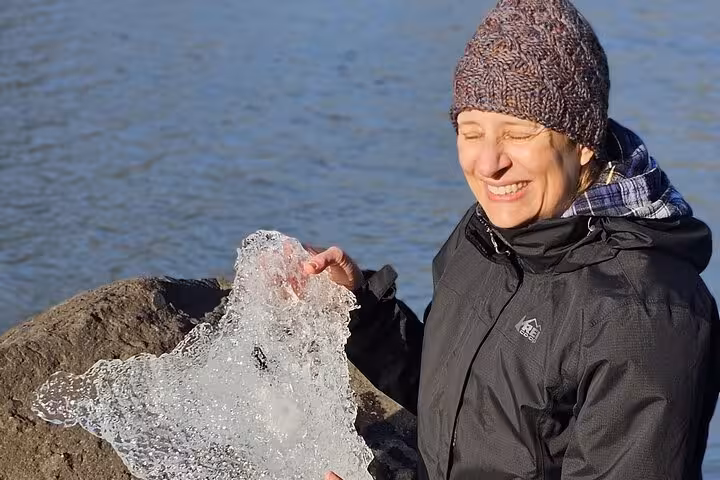 Smiling woman holding a piece of glacial ice on Iceland's south coast near rocky shoreline