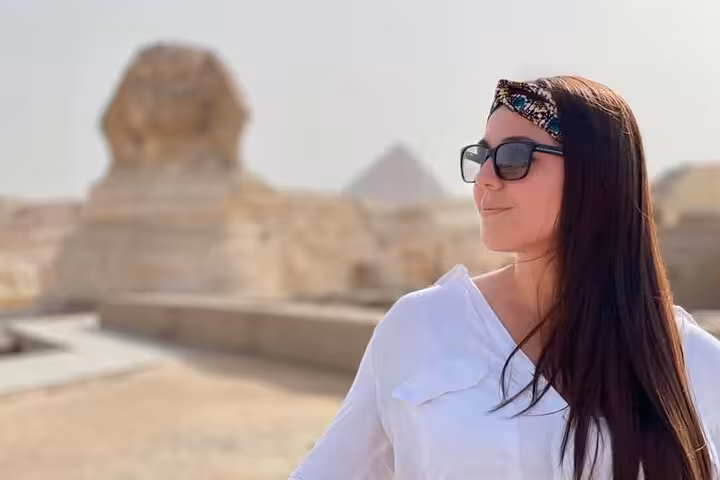 Woman in sunglasses near the Great Sphinx on a private Giza tour, pyramids blurred in the desert backdrop