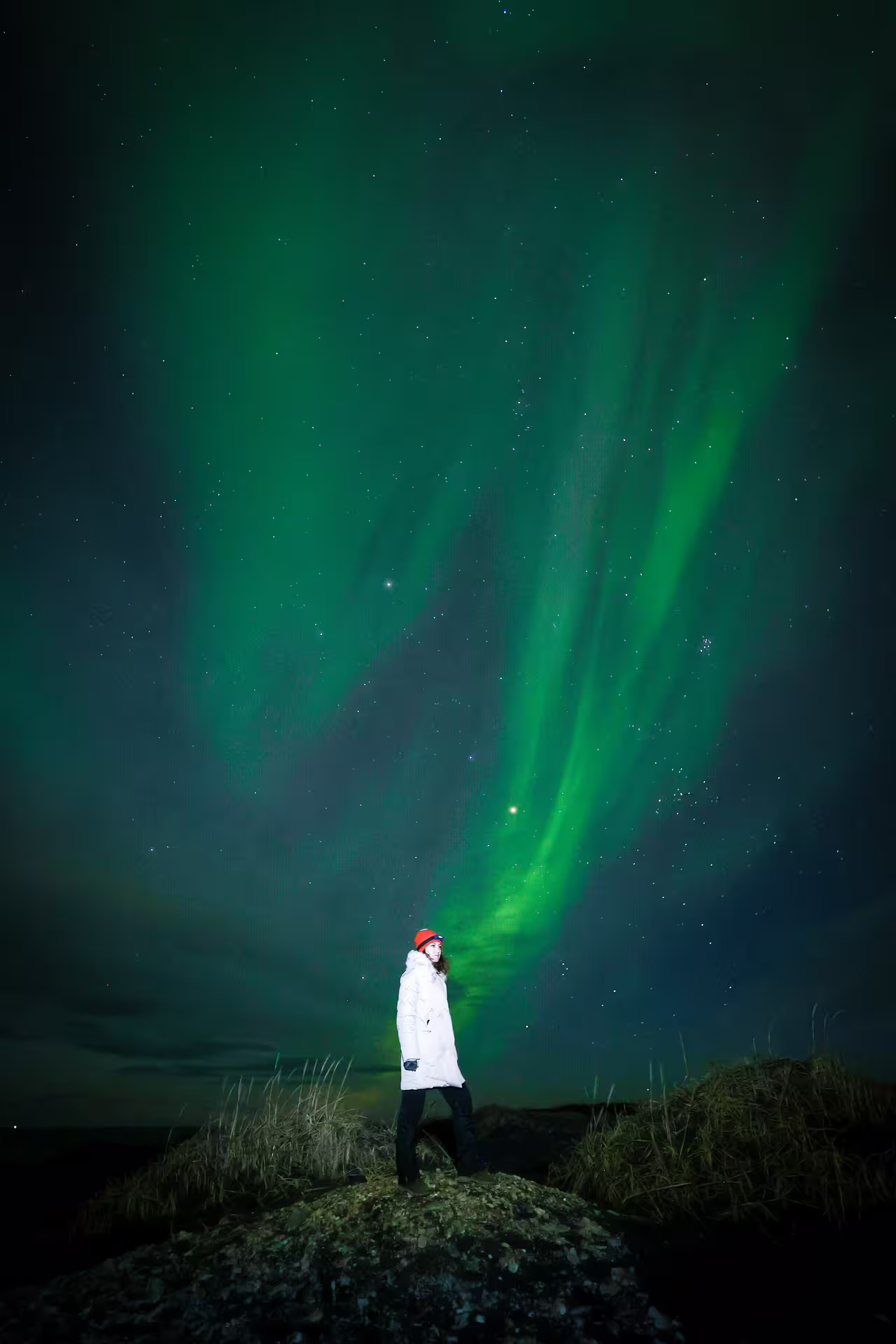 Woman standing on a rock beneath stunning green northern lights in Iceland during a private aurora photography tour