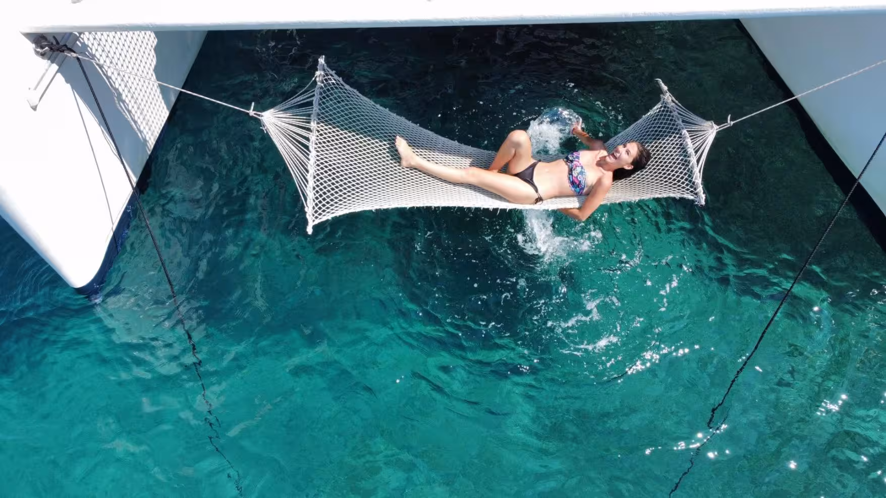 Woman lounging in a hammock over clear turquoise waters on a catamaran tour in Porto Conte Park, Alghero.