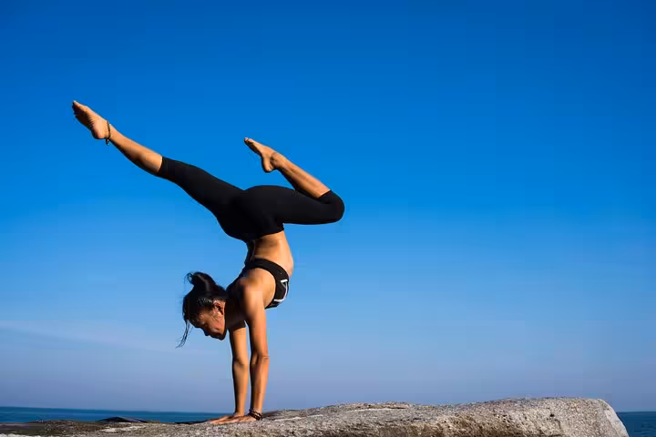 Woman practicing handstand yoga by the Santorini caldera, blue-sky seaside session for calm and mindfulness