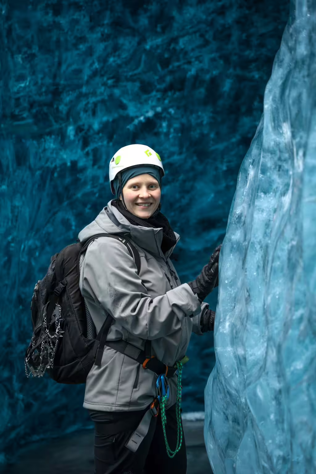 A smiling woman in a helmet touches ancient glacier ice walls during a private ice cave photoshoot adventure.