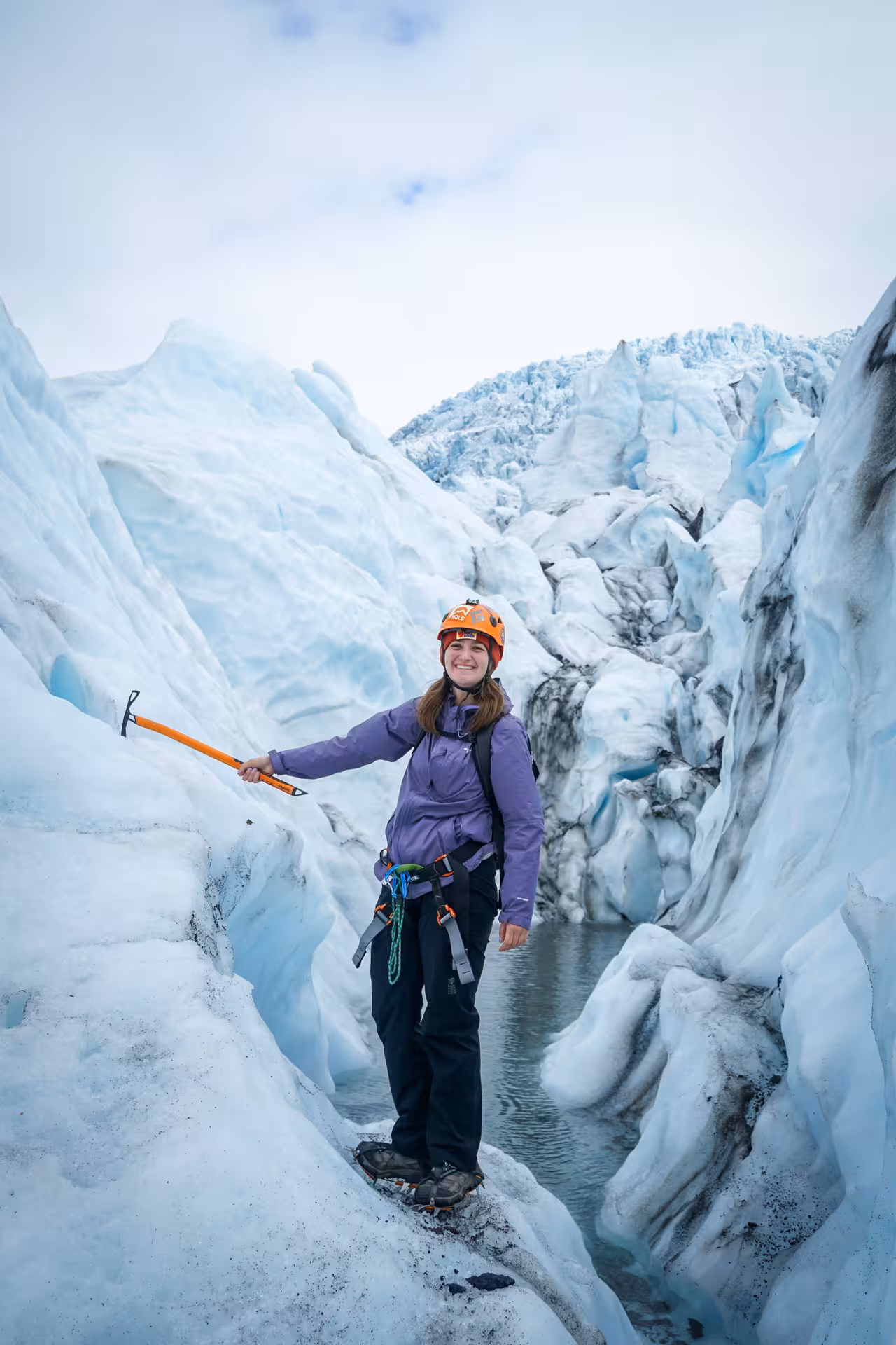 Woman hiker with ice axe and helmet exploring Iceland glacier crevasse on full-day guided hike