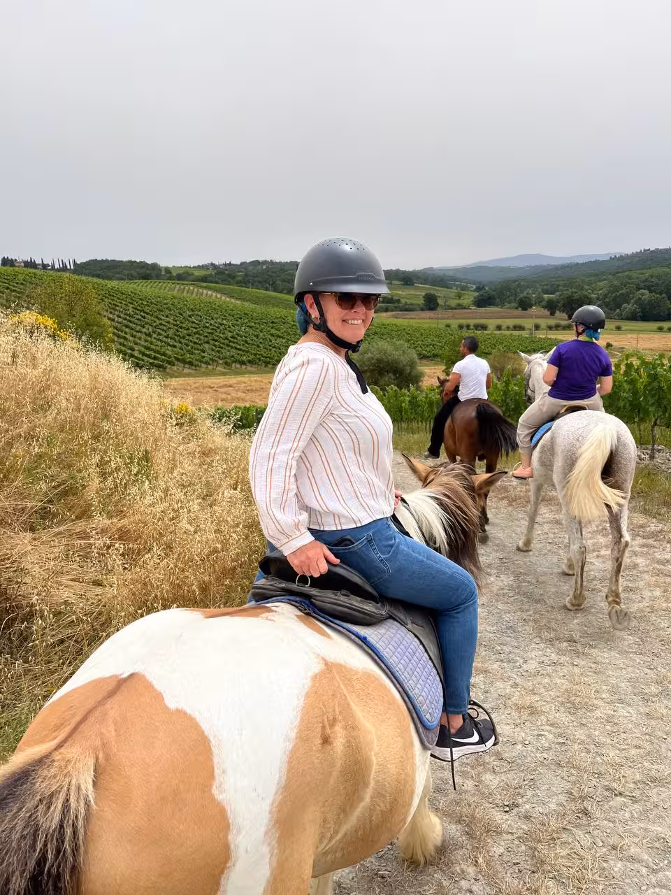 Smiling woman on horseback enjoying scenic Tuscany vineyard views during a guided riding tour.
