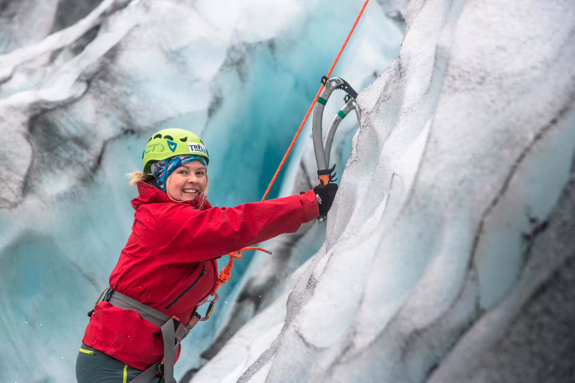 Smiling woman ice climbing on glacier wall with ice axe and safety harness in Skaftafell