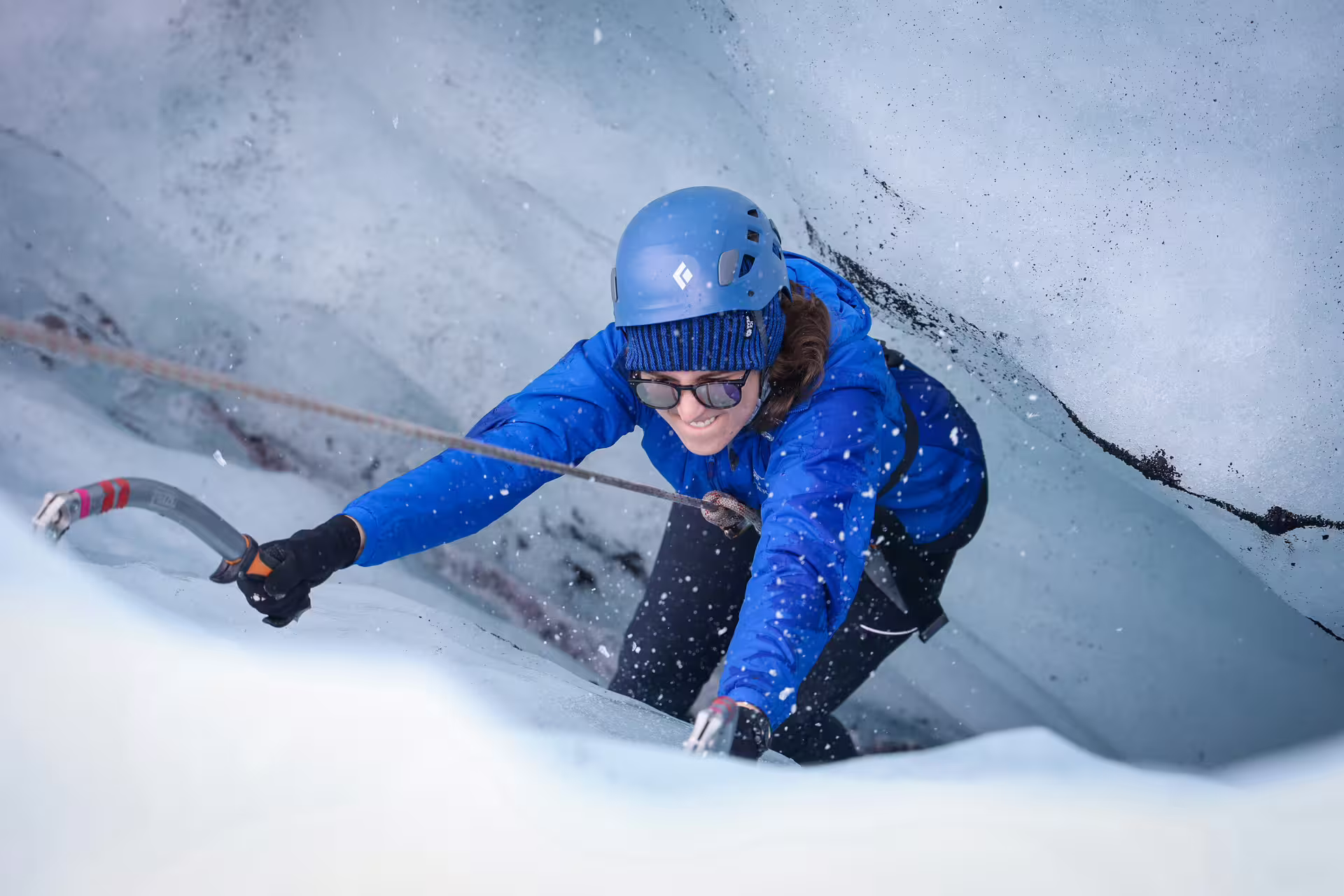 Woman ice climbing with axes and helmet scaling a glacial ice wall on a private Solheimajokull glacier tour