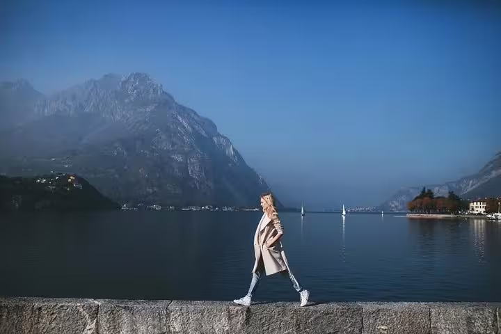 Woman walking along Lake Como waterfront with mountains and sailboats, private tour travel photographer session