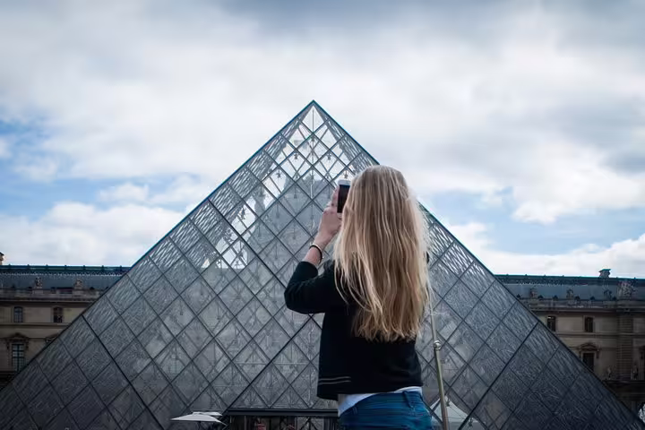 Woman photographing the iconic Louvre Pyramid in Paris, capturing the essence of hidden gems and undiscovered quarters.