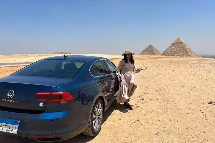 Woman posing by a car with the Pyramids of Giza in the background on a luxury private tour in Cairo.