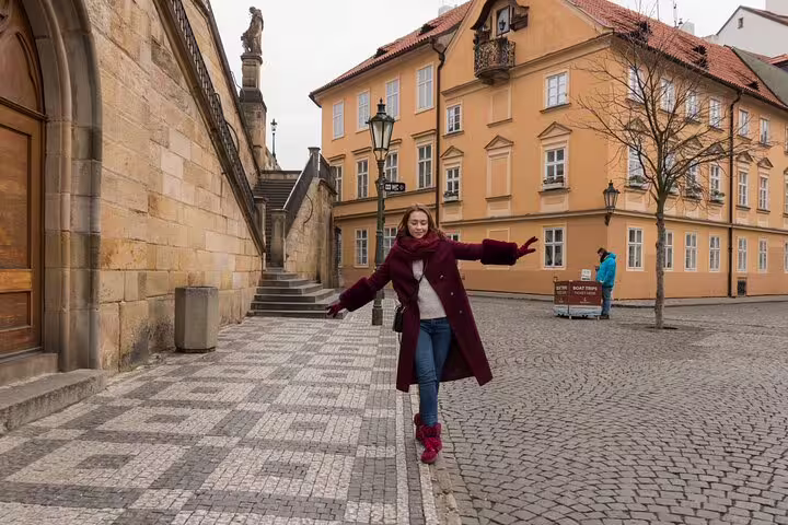 Woman in maroon coat joyfully walks along a charming cobblestone street in historic Prague during a private photoshoot.