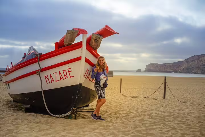 Woman posing by a traditional fishing boat on Nazaré beach, Portugal, part of a 3-day Lisbon World Heritage tour.