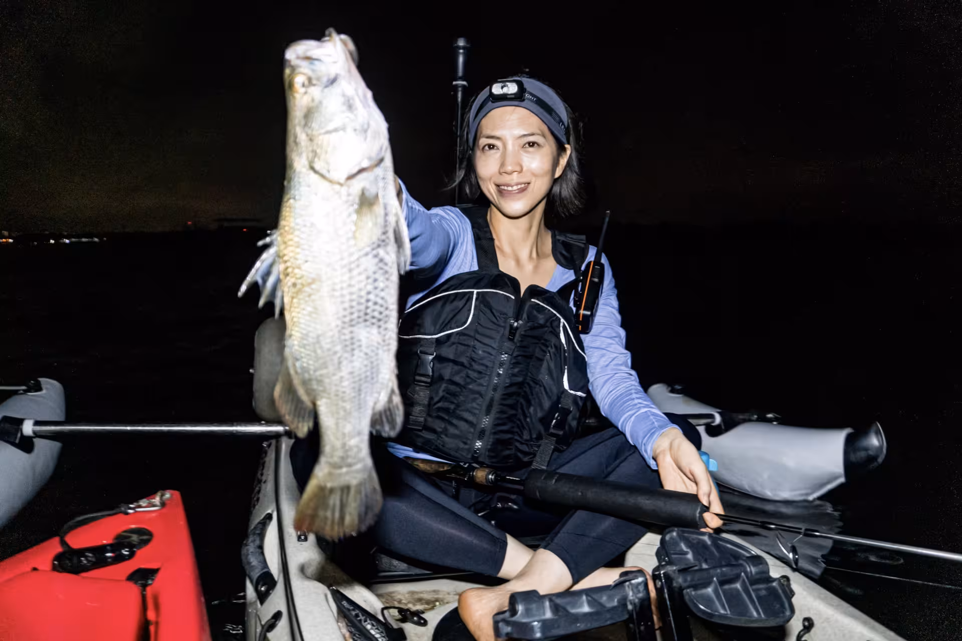 Woman proudly showcasing her catch during a night kayak fishing tour in Pulau Ubin, surrounded by serene waters.