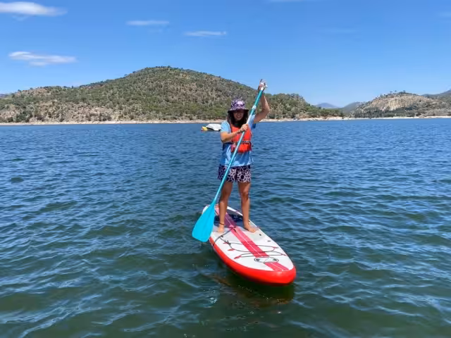 Woman stand up paddleboarding on a Teruel lake, guided SUP tour with clear water and forested hills under blue sky