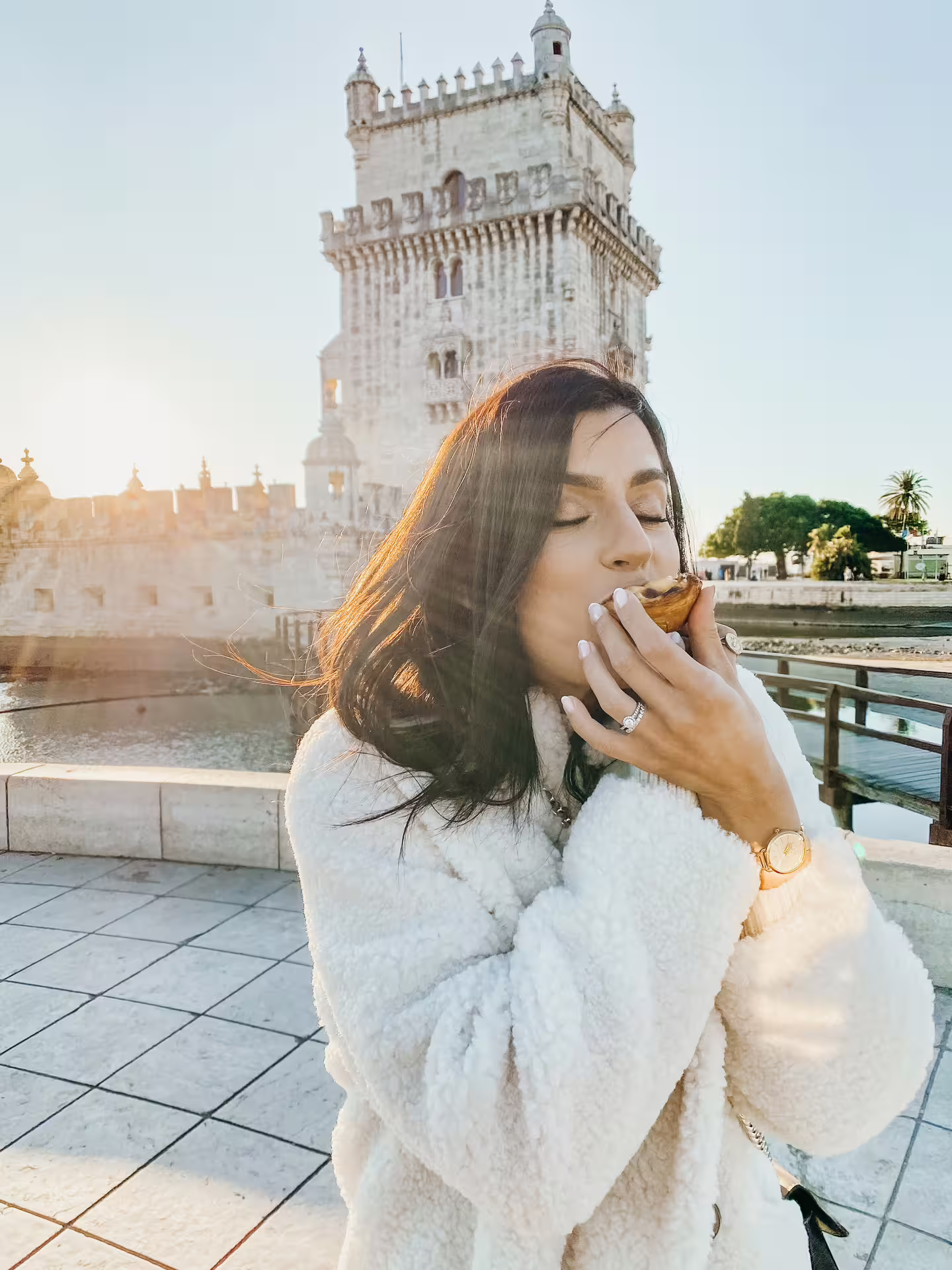 Woman enjoying a pastel de nata with Belém Tower in the background, capturing Lisbon's rich culinary heritage.