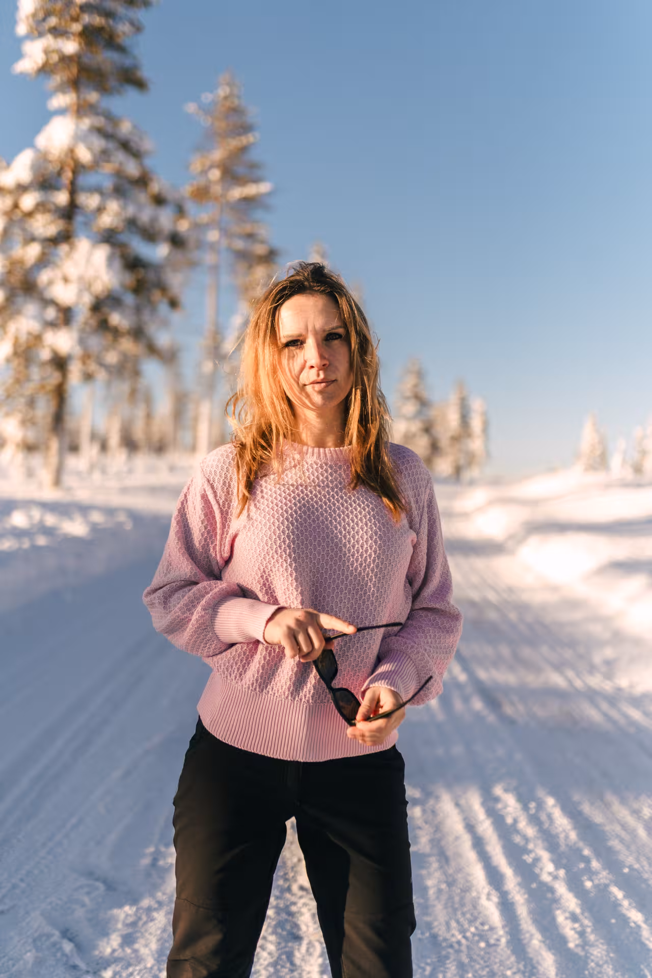 Woman in pink sweater enjoying a sunny winter day in snowy Rovaniemi forest, perfect for holiday photo sessions.