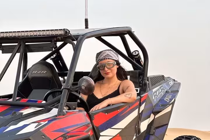 Woman in goggles seated in Polaris RZR dune buggy on sand dunes, ready for off-road desert quad tour