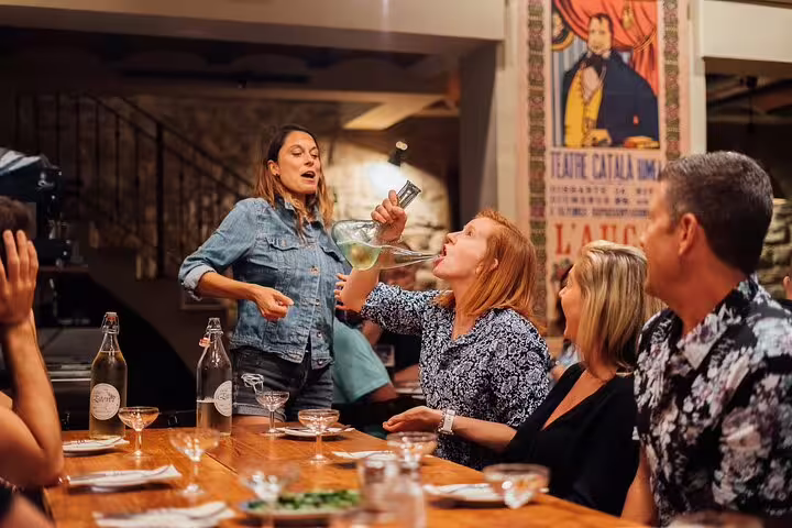 Woman pours wine from a porron during lively private tapas tour in Spanish restaurant.