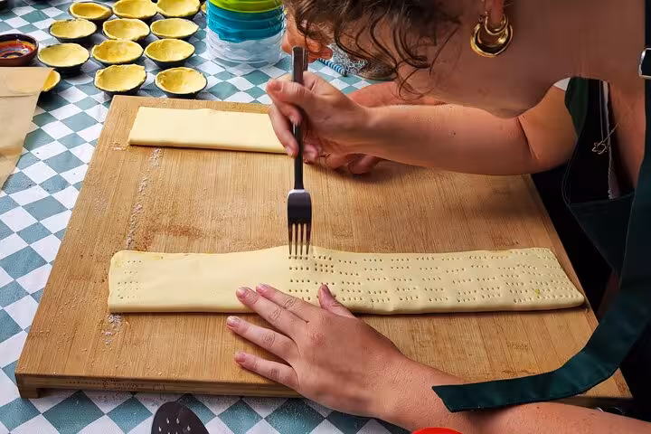 Woman preparing pastry dough for pastel de nata on a checkered table, showcasing traditional Portuguese baking.