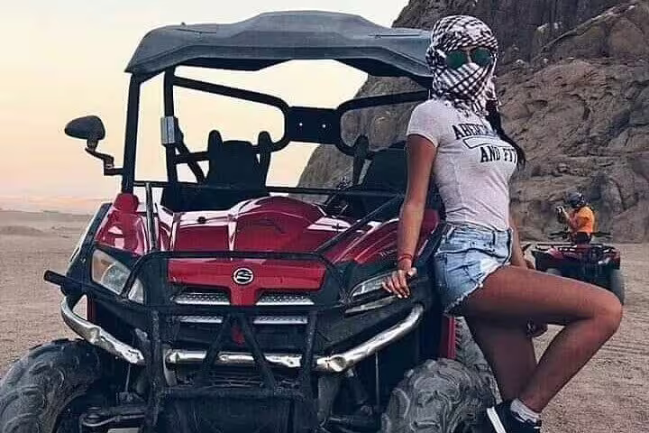 Woman posing beside red buggy during Sharm El Sheikh desert safari tour near Sinai mountains at sunset