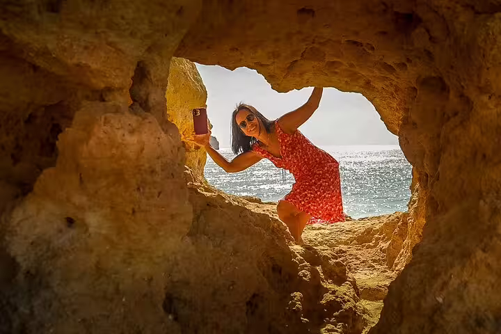 Woman in a red dress exploring the scenic Benagil caves on a sunny Algarve private tour, capturing memories by the sea.