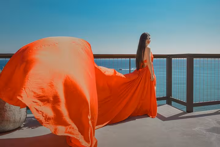 Elegant woman in vibrant red dress overlooks the sea in Hersonissos flying dress photoshoot experience.