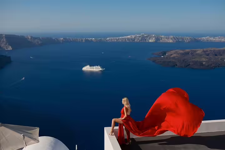 Woman in flowing red dress overlooking Santorini caldera, capturing stunning private photography experience.