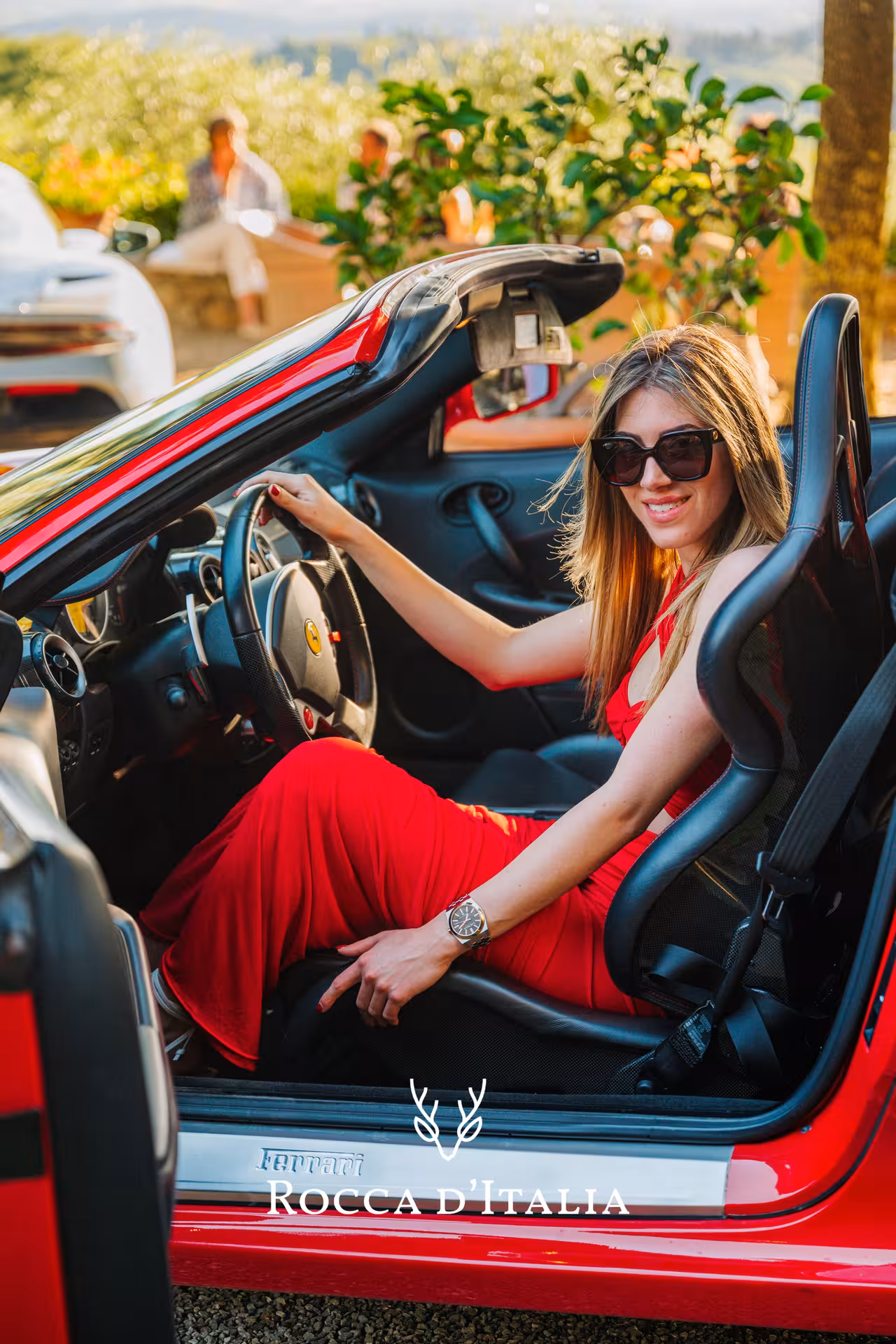 Woman in red dress sitting in open-top red Ferrari supercar in Siena Tuscany countryside