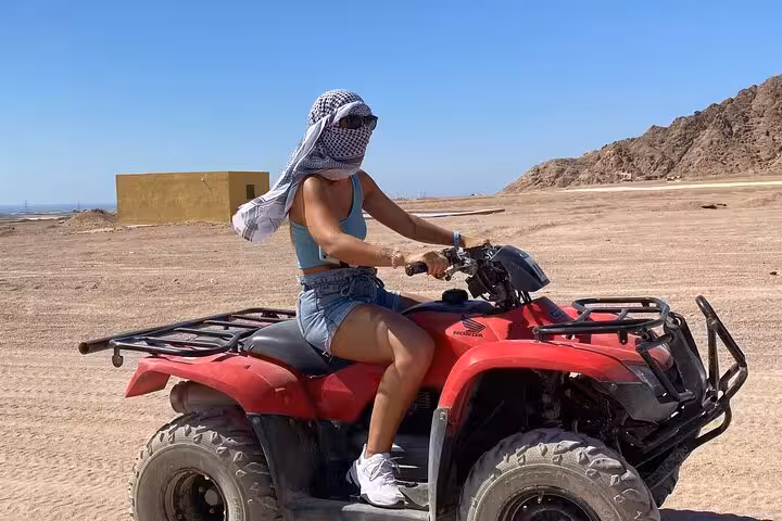 Woman riding a red quad bike in Sinai desert on a private VIP Sharm El Sheikh ATV safari with guide