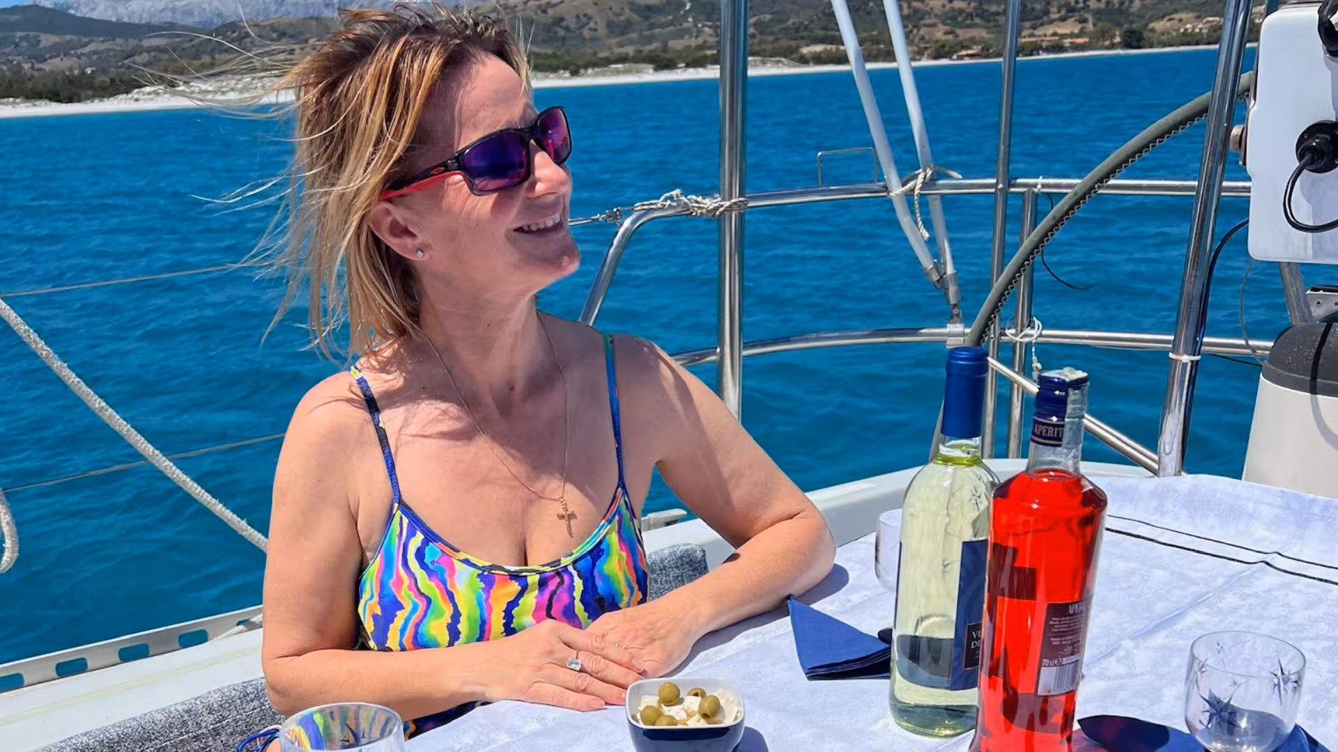 Woman relaxing with drinks on a sailing boat in San Teodoro, capturing the essence of a Sardinia sailing tour.