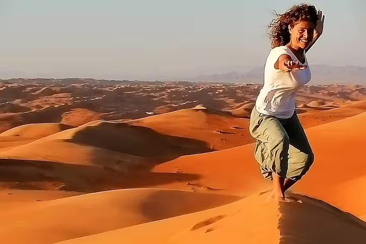 Woman joyfully balancing on sand dune in Wahiba Sands during a 2-day private desert camping tour from Muscat.