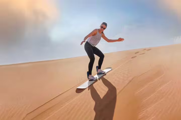 Woman sandboarding down a golden dune during a Dubai desert safari adventure.