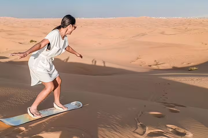 Woman sandboarding down a golden dune in Dubai, showcasing adventure during a private desert safari experience.