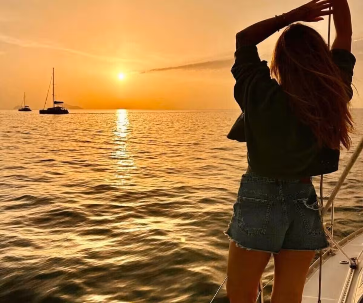 Woman watching the Santorini sunset from a private sailing cruise, with catamarans on the calm Aegean Sea