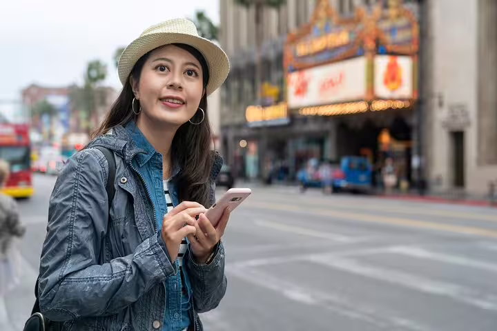 Young woman holding smartphone on Hollywood Boulevard at night, exploring city streets