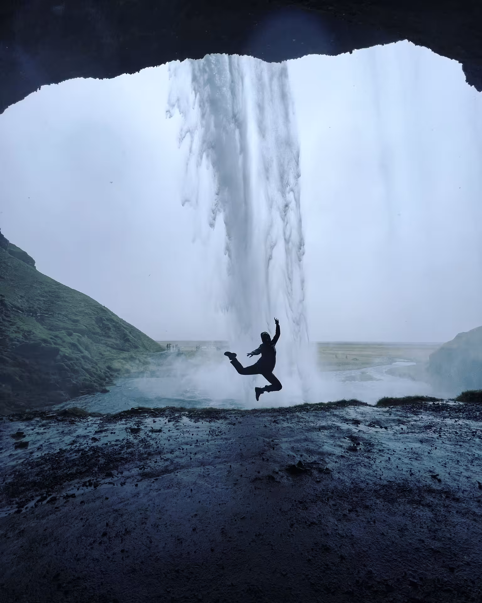 Woman jumps joyfully behind Seljalandsfoss waterfall, experiencing Iceland's natural wonder on New Year's Eve adventure.
