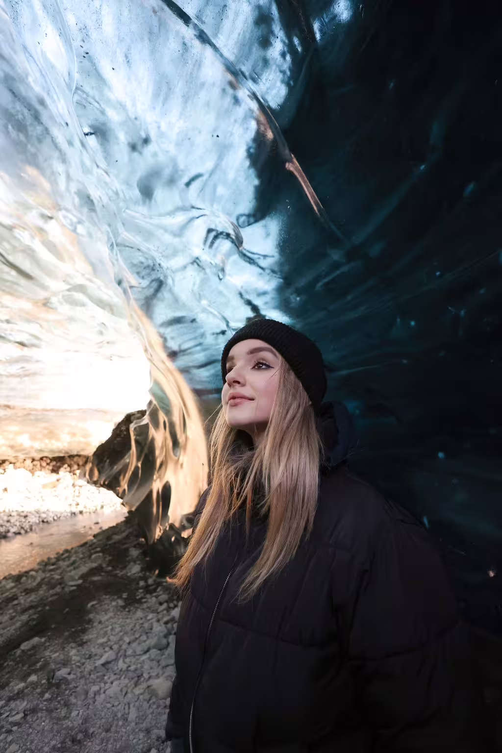 A woman in a black jacket and beanie smiles inside a stunning Iceland glacier ice cave on a private early bird tour.