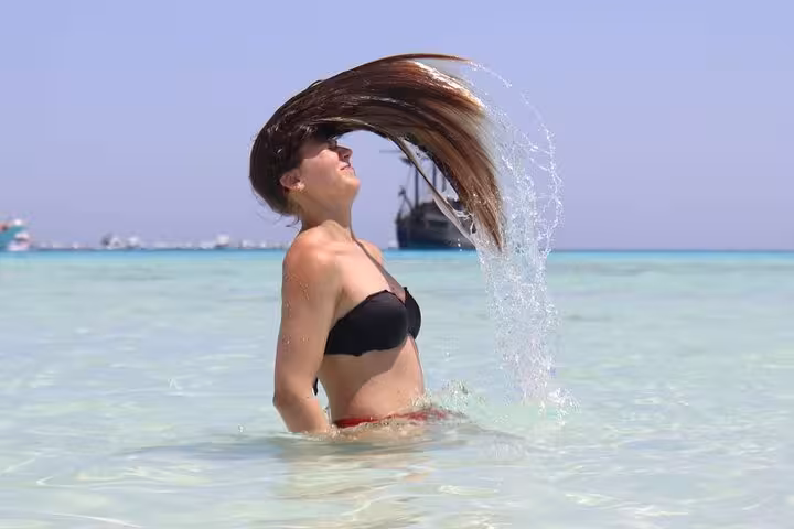 Woman flipping hair in crystal-clear shallows at White Island, Ras Mohamed snorkeling day trip from Sharm El-Sheikh