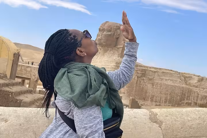 Woman playfully poses with the Great Sphinx in Giza, showcasing a fun moment on a private tour with camel rides.