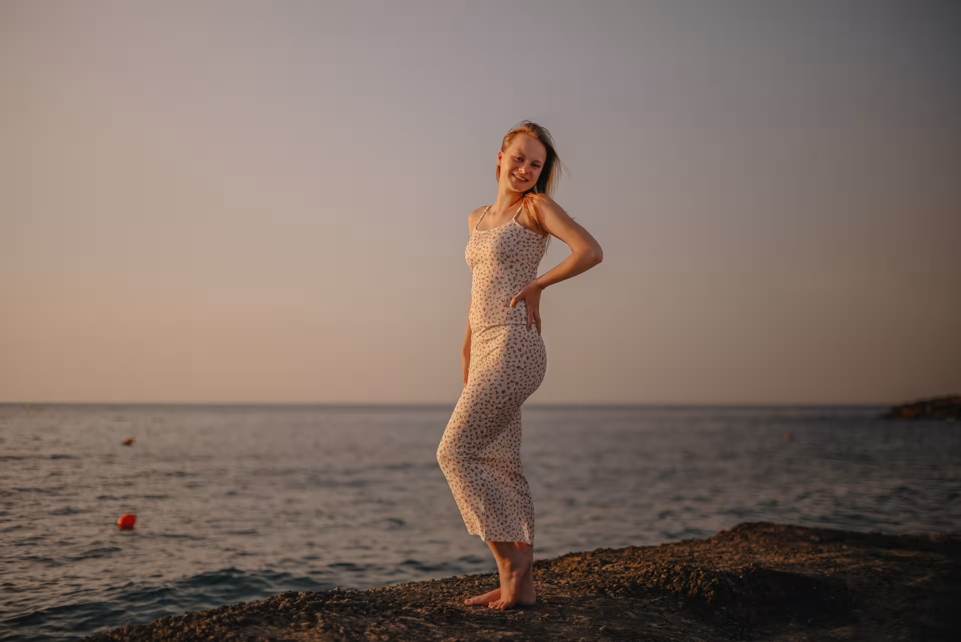Smiling woman in a sundress posing at sunset by the sea in Analipsi during a private photoshoot session.