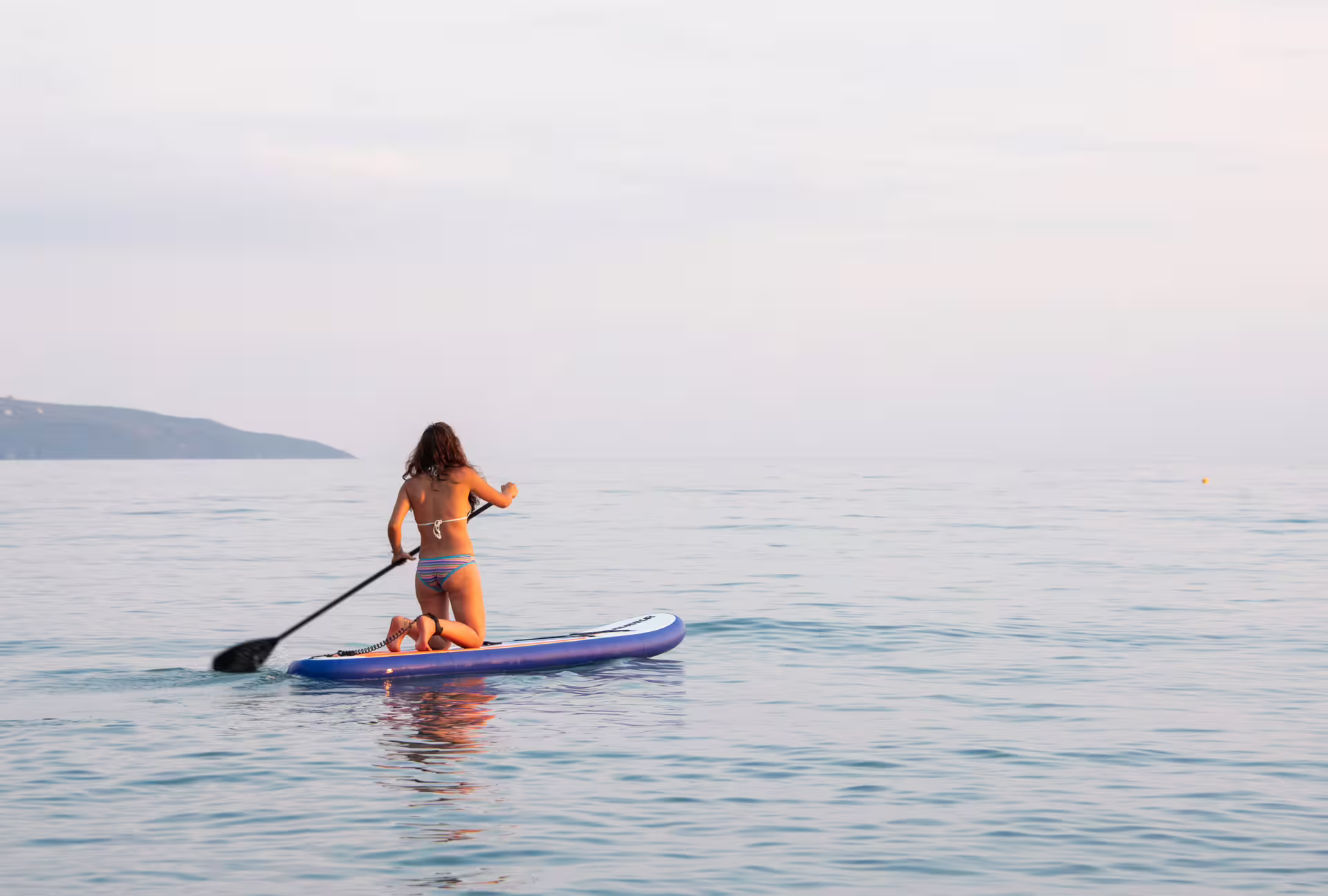 Woman kneeling on a SUP board paddling calm waters near Kardamyli, Messinia, Greece stand up paddle tour