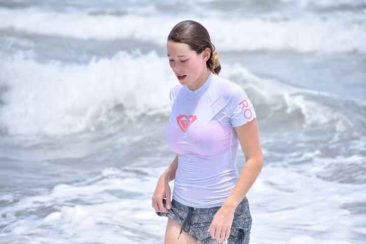 Woman in white rash guard enjoying the waves during a surf lesson in Manuel Antonio, Costa Rica.