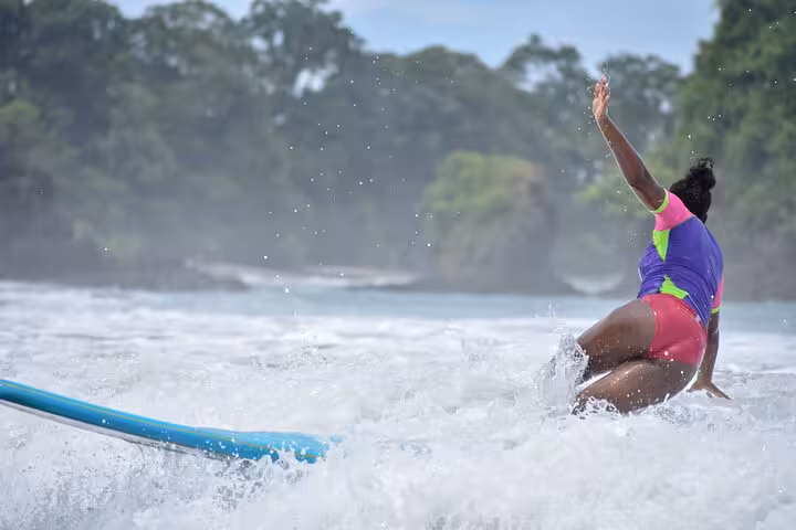 Woman in vibrant wetsuit learning to surf on Manuel Antonio's lively waves, capturing the thrill of Costa Rica surfing.