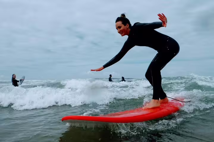 Woman surfing on a red board at Lisbon beach, enjoying an exhilarating surf experience with overcast skies and waves.