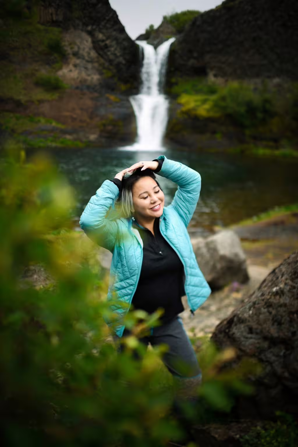 A smiling woman in a teal jacket poses before a stunning Iceland waterfall on a 12-day grand tour.