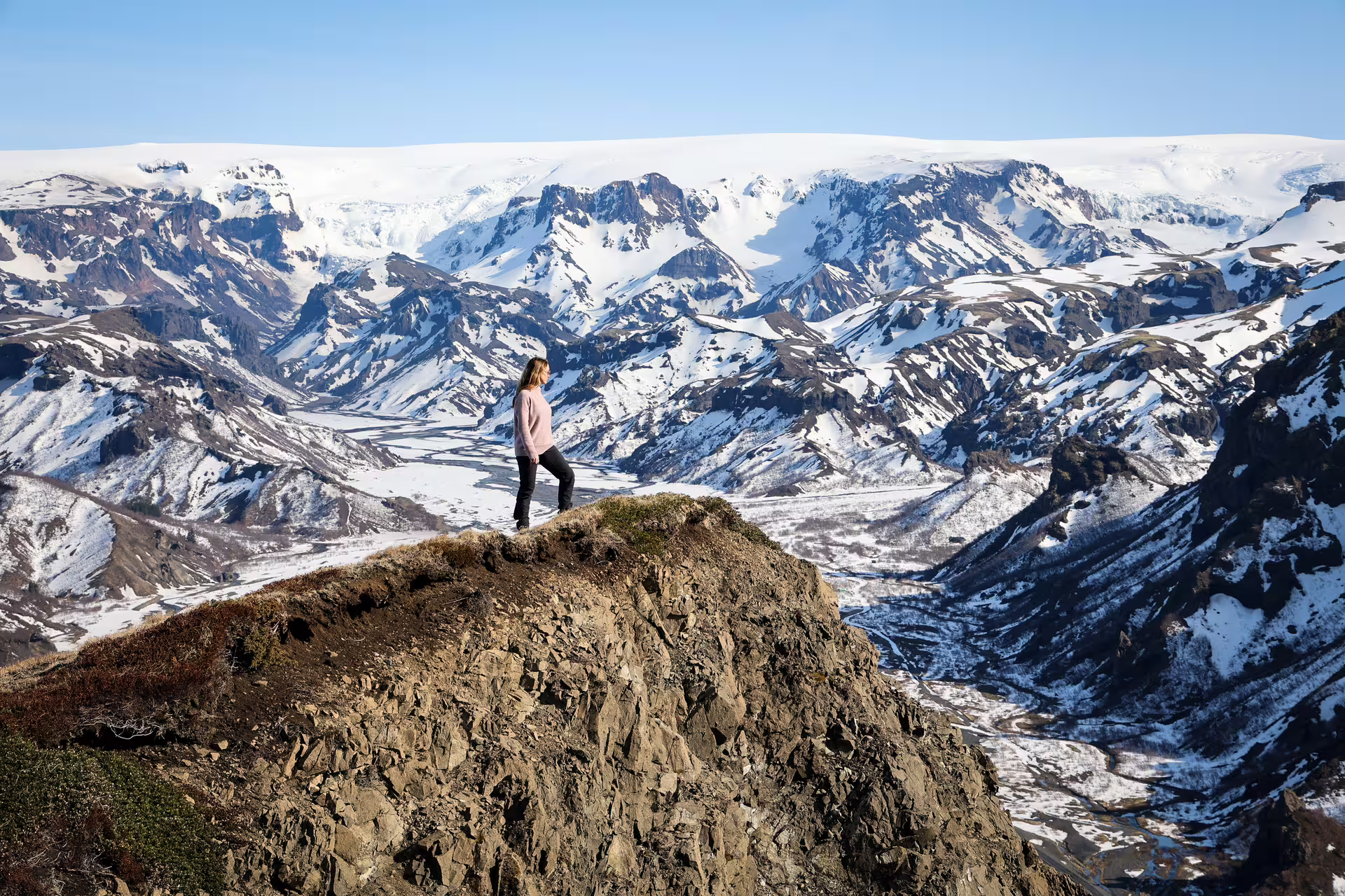 Woman standing on a rocky summit overlooking Thorsmork's snow-capped valley on a full-day 4x4 tour from Reykjavik Iceland