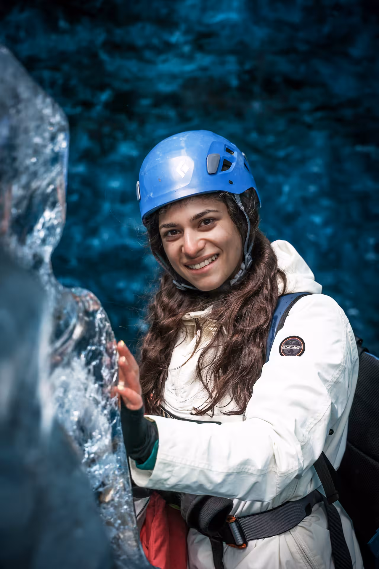 Smiling woman in blue helmet touches ancient ice wall during Falljokull glacier hike photo shoot tour in Iceland