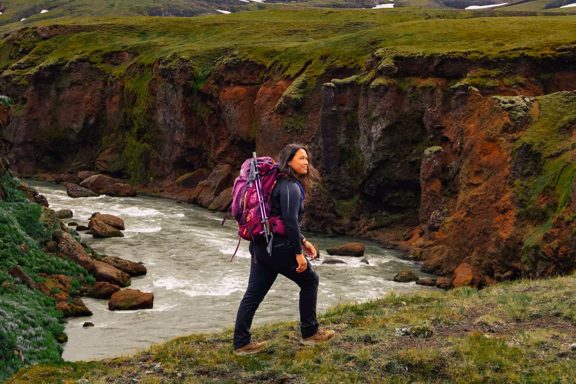 Woman hiking with purple backpack along glacial river canyon on Laugavegur trail, Iceland
