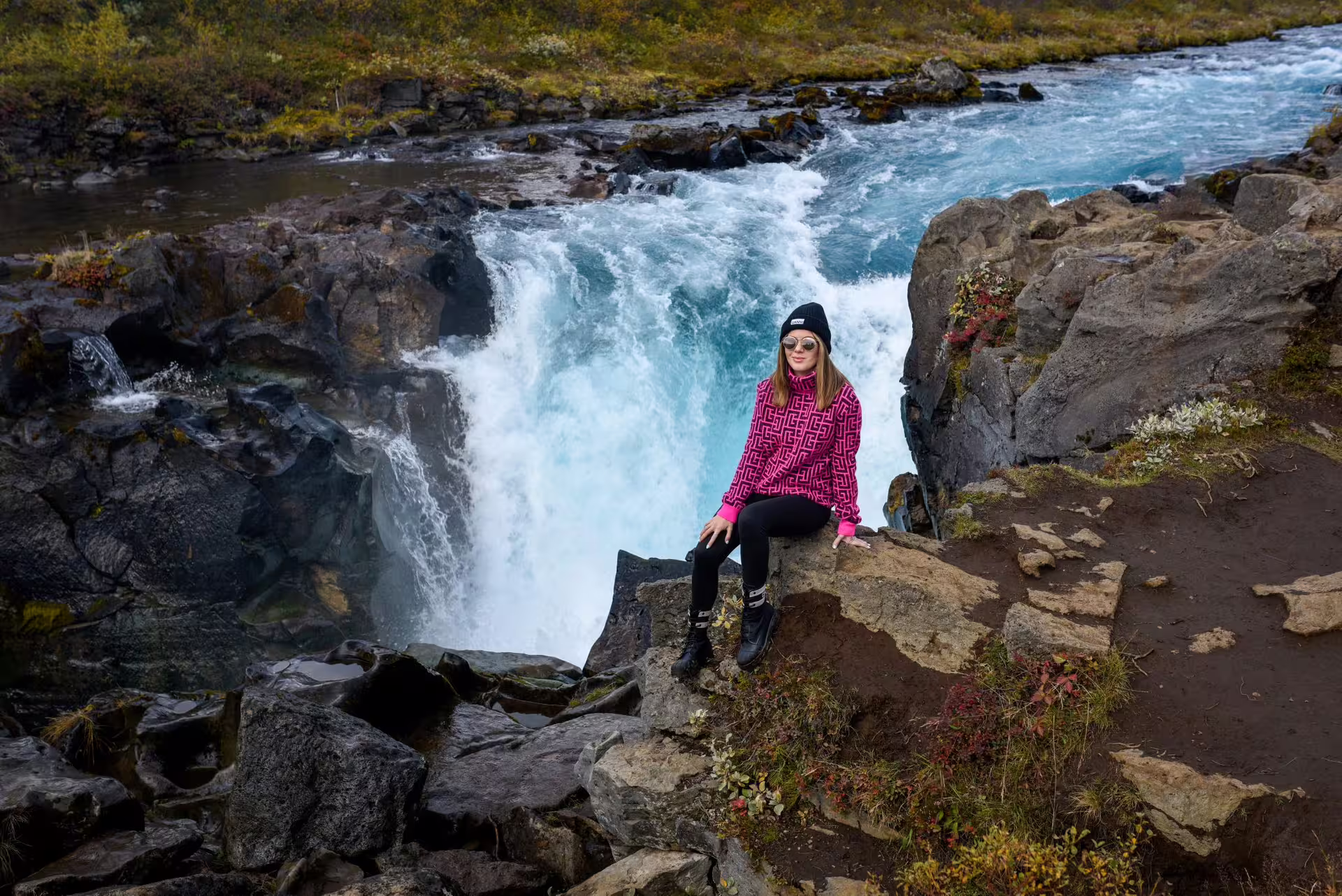 Woman sitting on rocks beside a powerful turquoise Icelandic waterfall on a private Golden Circle day tour with photographer