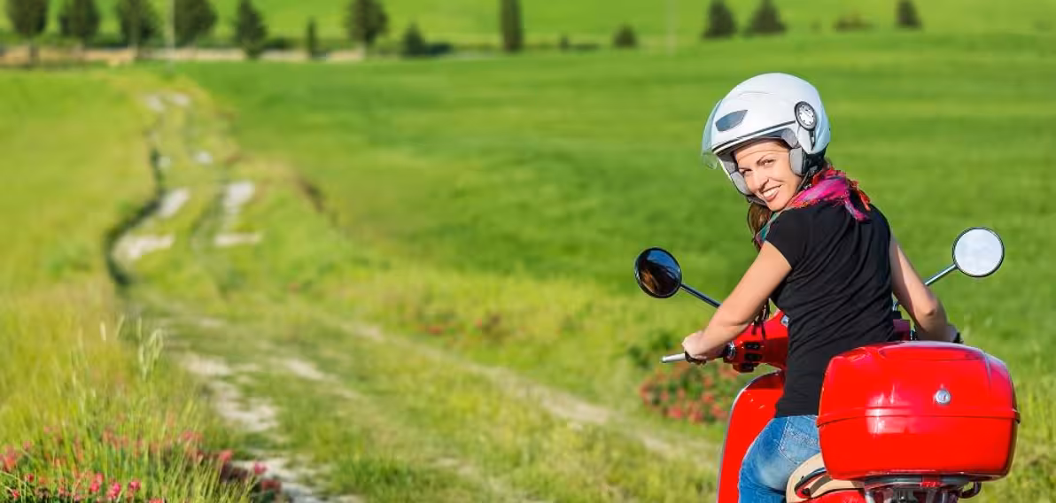 Woman enjoying Tuscany countryside on a Vespa tour from Florence, surrounded by lush green landscapes.
